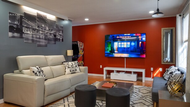 A modern living room with a sofa, ottomans, a coffee table, and a flat-screen TV mounted on the wall. - Urban Edition (Long Pond)