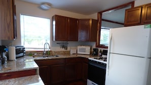 A kitchen with wooden cabinets, a granite countertop, a sink, a stove, and a refrigerator. - Cedar Haven Rolla - Relax in comfort close to downtown! (Rolla)