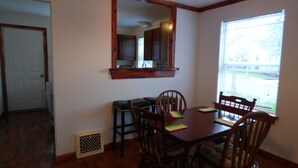 A dining room with a wooden table, four chairs, a mirror, and a window with blinds. - Cedar Haven Rolla - Relax in comfort close to downtown! (Rolla)