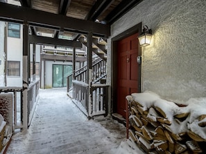Staircase leads to a cozy entrance with a red door and firewood nearby.