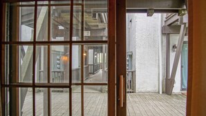 Une terrasse en bois offrant une vue sur l’intérieur d’un bâtiment, visible à travers une porte vitrée.