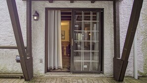 Une terrasse en bois menant à un bâtiment doté d’une porte-fenêtre coulissante et d’un petit luminaire extérieur.