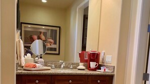 A bathroom with a vanity, sink, mirror, and a coffee maker.