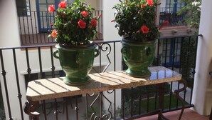 Two green planters with red flowers on a balcony with a tiled floor and metal railing.