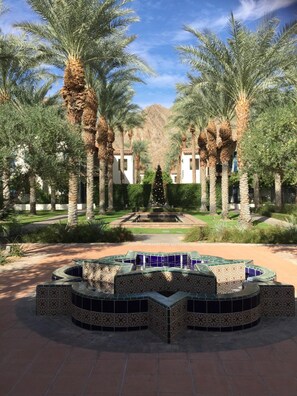 Stroll through a serene courtyard surrounded by palm trees and a central seating area, flanked by buildings with terracotta roof tiles.