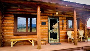 Une cabane en rondins dotée d’une grande fenêtre, d’une porte ornée d’une sculpture représentant un élan et d’un banc à l’extérieur.