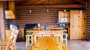 Une cabane en bois rustique, avec une grande table et des bancs en bois, un poêle, un four à micro-ondes et un évier.