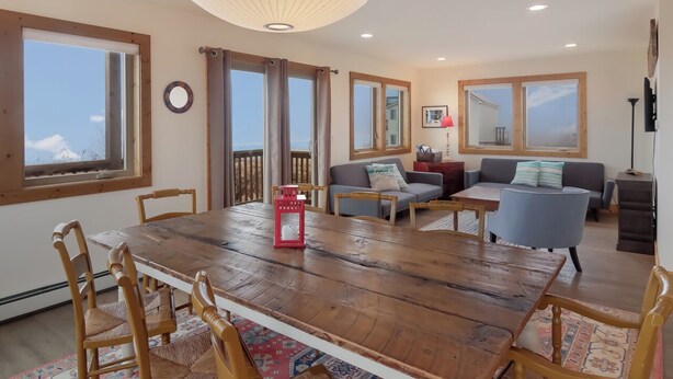 Een ruime woonkamer met een houten eettafel, een bank en een balkon met gordijnen.