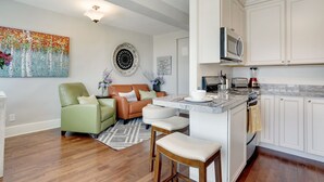 A modern kitchen with white cabinets, a built-in microwave, and a dining area with a green sofa and a coffee table. - Stadium District Room With A View (Tacoma)