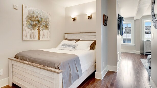 A bedroom with a wooden bed, a painting of a tree, and a hallway leading to another room. - Stadium District Room With A View (Tacoma)