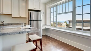 A modern kitchen with white cabinets, a stainless steel refrigerator, a marble countertop, and a large window offering a view of the city. - Stadium District Room With A View (Tacoma)