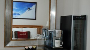 Une chambre d’hôtel avec un grand miroir reflétant un paysage de montagne enneigée, une machine à café et un lit avec un oreiller rouge.