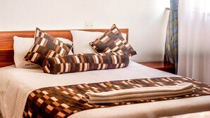 A neatly made bed with patterned pillows and a woven blanket, a wooden headboard, and a white wall with a power outlet. - Furnished Studio Apartments at YWCA Parkview Suites ,Nairobi(YWCA OF KENYA) (Nairobi)