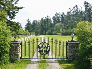 Enter a serene oasis through the beautifully landscaped entrance, flanked by stone pillars and a decorative metal gate.