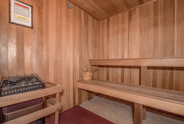 Un sauna en bois avec des bancs, un appareil de chauffage pour sauna et un panneau d’avertissement.