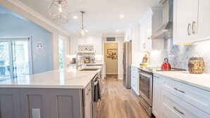 Une cuisine moderne dotée d’un grand îlot central, d’appareils électroménagers en acier inoxydable et de luminaires suspendus.