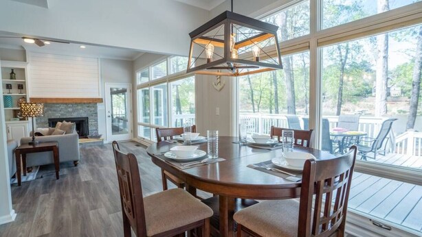 Un vaste espace dédié à la salle à manger, avec une grande table et des chaises en bois, un luminaire suspendu et de grandes fenêtres offrant une vue sur l’extérieur.