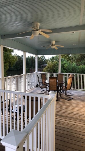 Une terrasse extérieure couverte, dotée d’une table et de chaises, d’un ventilateur de plafond et offrant une vue sur une étendue d’eau.