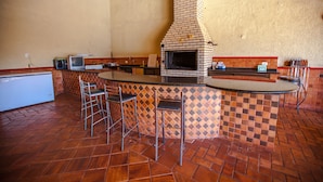 A kitchen with a brick oven, bar stools, and a tiled backsplash. - Foz Temporada (Foz do Iguaçu)