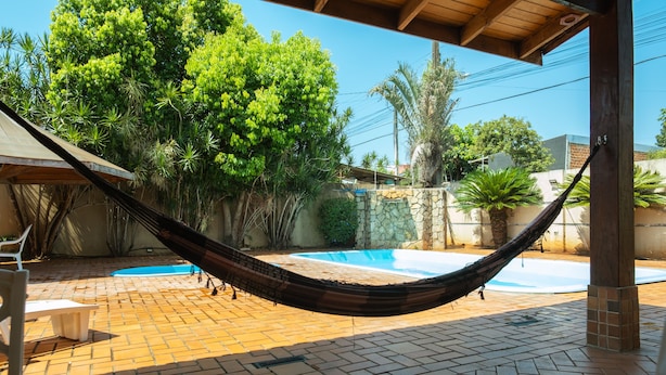 A hammock over a brick patio with a pool and lush greenery. - Foz Temporada (Foz do Iguaçu)