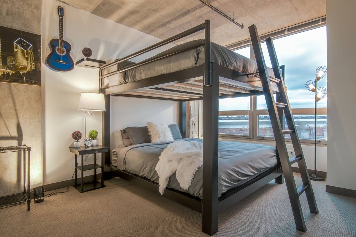 A bunk bed with a ladder, a desk with a lamp, and a guitar on the wall.