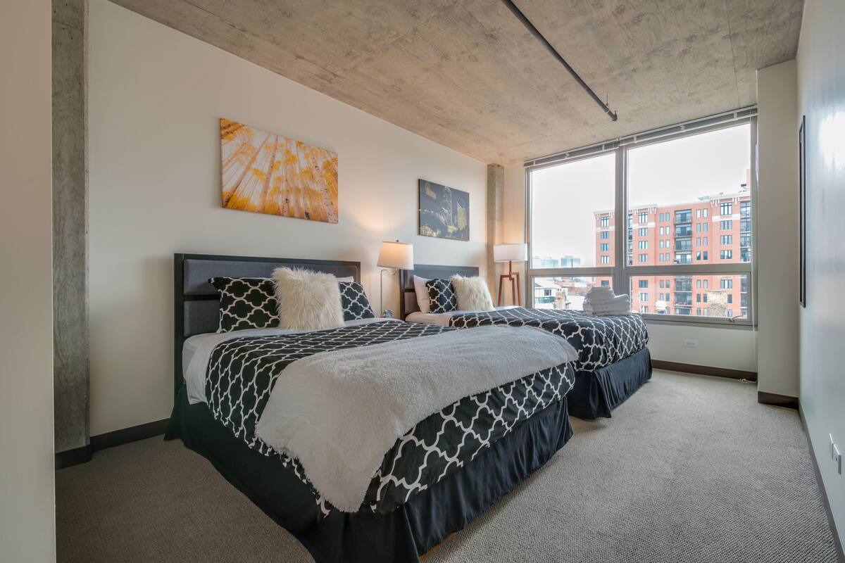 A hotel room with two beds, a large window, and artwork on the walls.