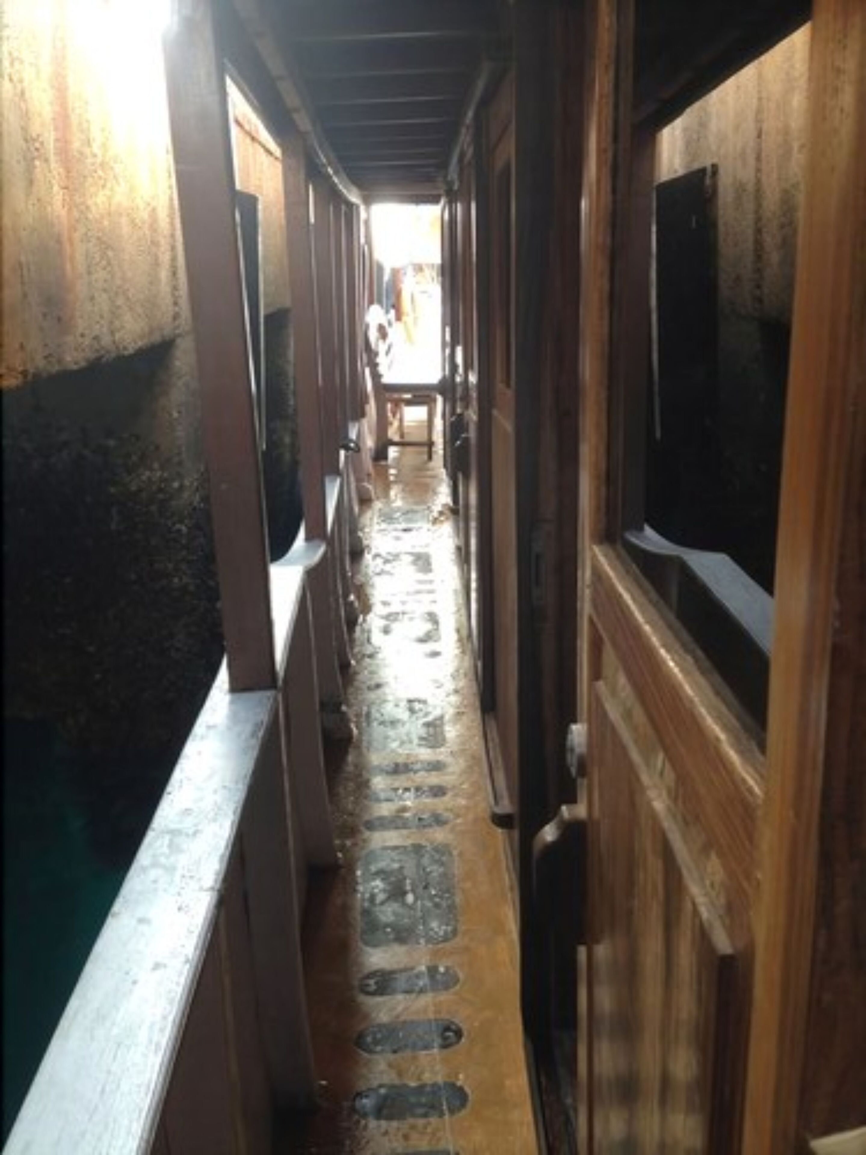 A narrow corridor with wooden walls and a metal railing on one side.
