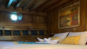 A wooden cabin-style room with a bed, a painting on the wall, and a ceiling light fixture.