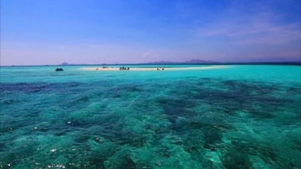 A clear view of a beach with turquoise water and a distant island.