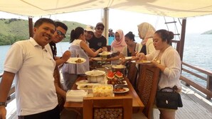 A group of people dining on a boat with a table full of various dishes.
