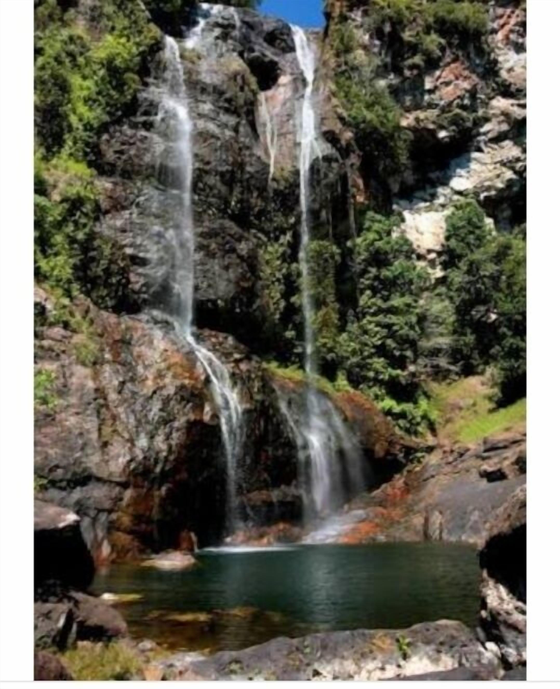 A waterfall cascading into a pool surrounded by rocky terrain and greenery.