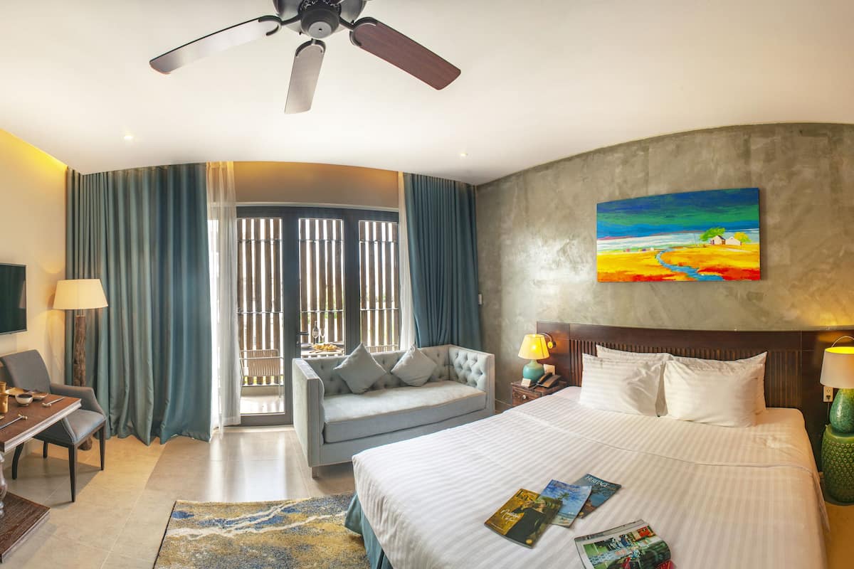 Une chambre d’hôtel équipée d’un lit, d’un bureau, d’une chaise, d’une télévision, d’un tableau et d’un ventilateur de plafond.