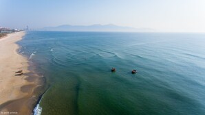 Luchtbeeld van een strand met helder water, boten en verre bergen.