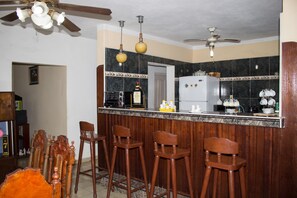 A kitchen with a bar area, wooden chairs, a refrigerator, and a ceiling fan. - Mar Azul (Cienfuegos)