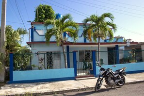 A two-story building with a blue and white exterior, a motorcycle parked in front, and a palm tree in the foreground. - Mar Azul (Cienfuegos)