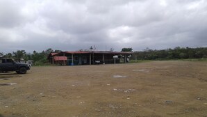 A rural building with a dirt ground and a parked vehicle. - Tripsyala (Ailigandí)