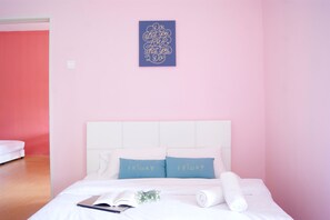 Un dormitorio con una cama blanca, dos almohadas con el texto "FRIDAY", un cuadro azul en la pared y un cabecero blanco.