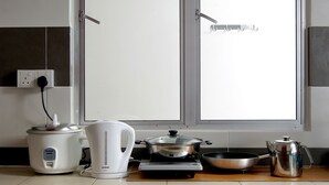 A kitchen with a white electric kettle, a rice cooker, a frying pan, and a stainless steel pot on a countertop. - PLAY Residence at Cameron Jaya (Tanah Rata)