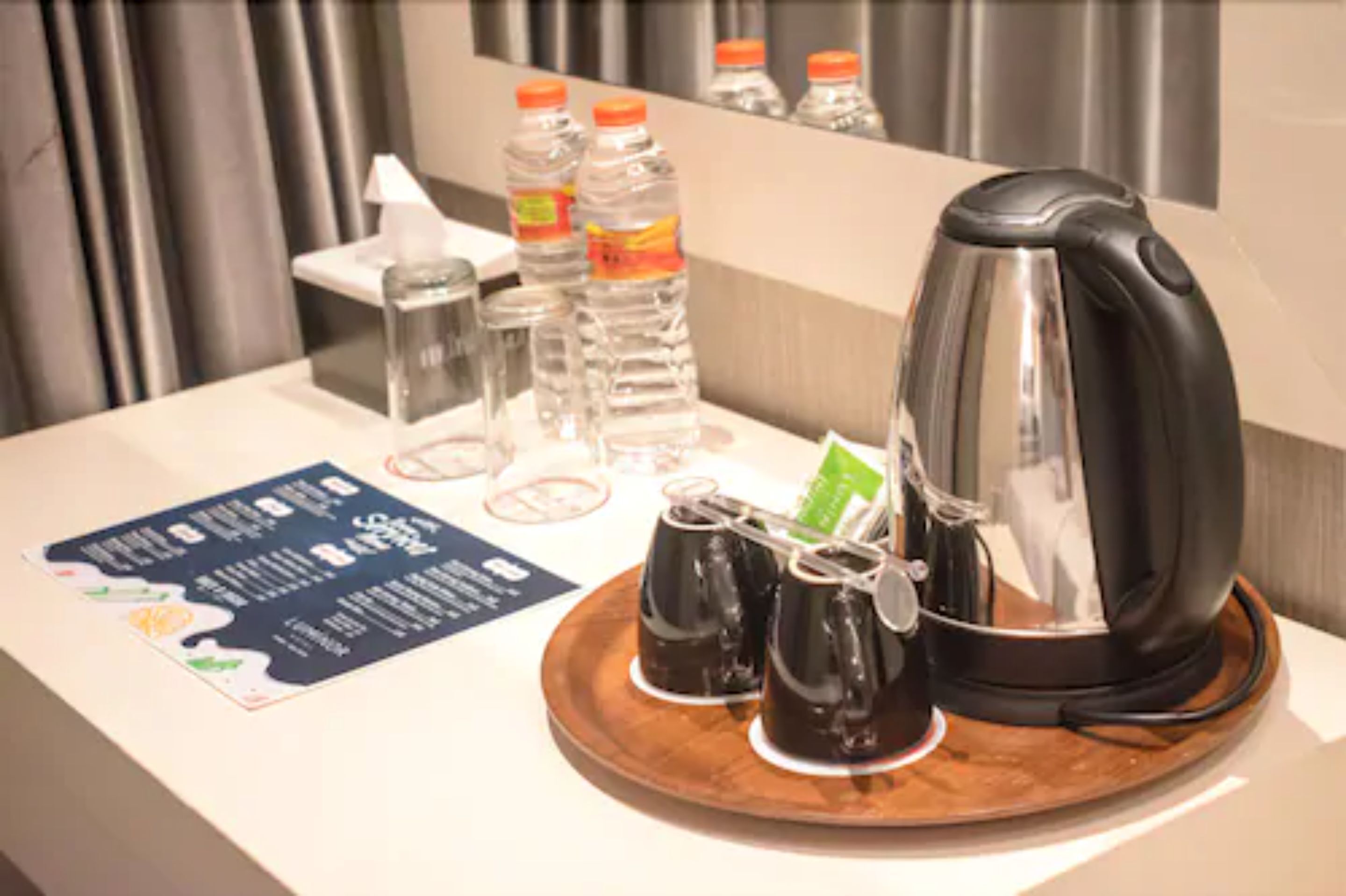 A hotel room's breakfast setup with a coffee maker, two cups of coffee, a tray with condiments, and water bottles.