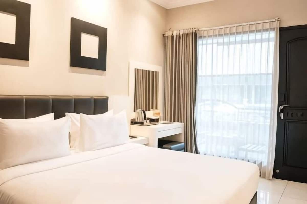 Una habitación de hotel con una cama grande, un escritorio, una silla, un espejo y una puerta.