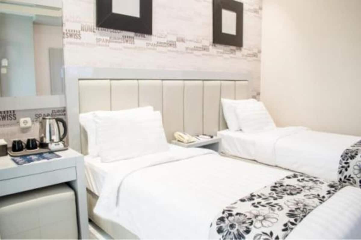 Habitación de hotel con dos camas, una mesita de noche con teléfono y hervidor, y una pared decorada con cuadros.