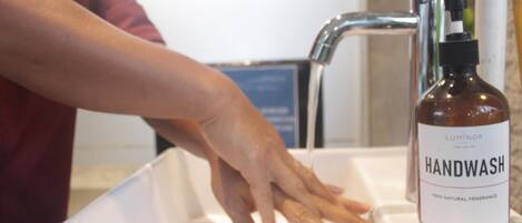 A hand under a faucet with a bottle of handwash on the sink.