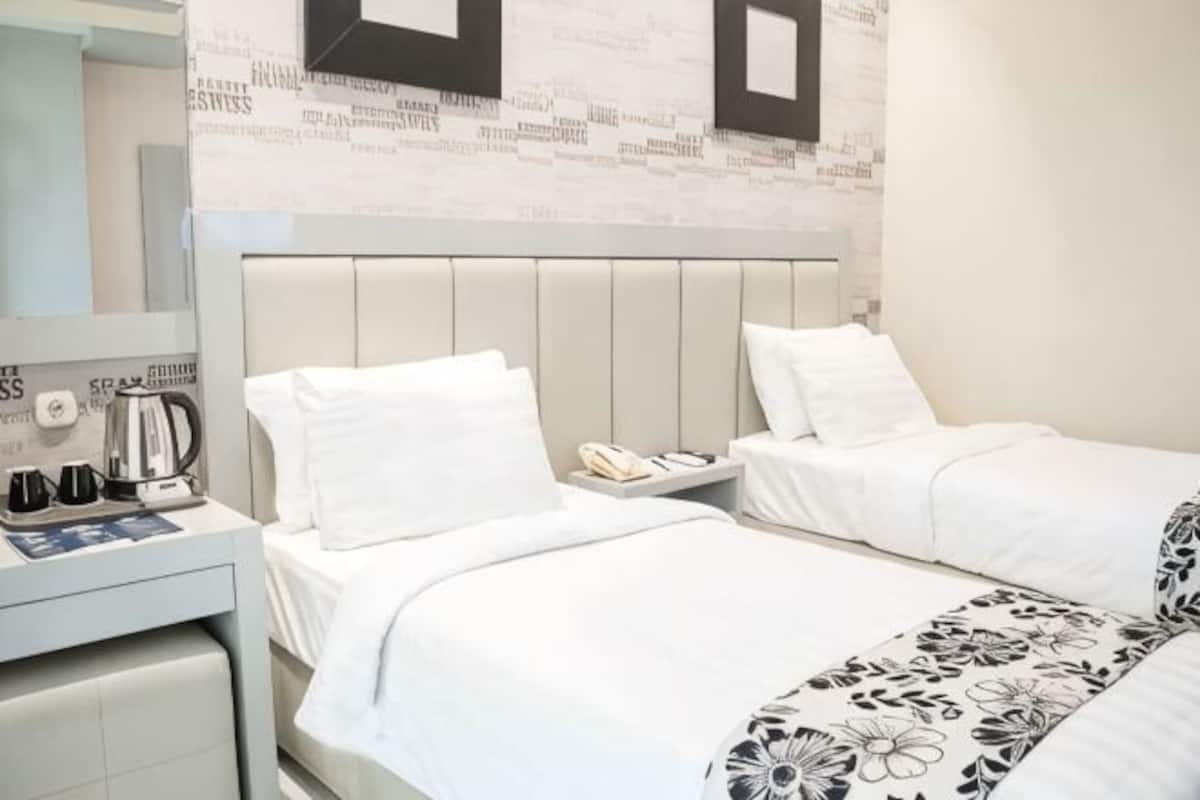 Una habitación de hotel con dos camas, un escritorio con teléfono y un espejo.