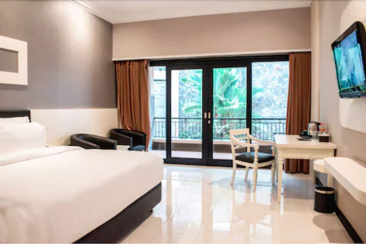 Habitación de hotel con una cama grande, un escritorio, una silla y un televisor en la pared.