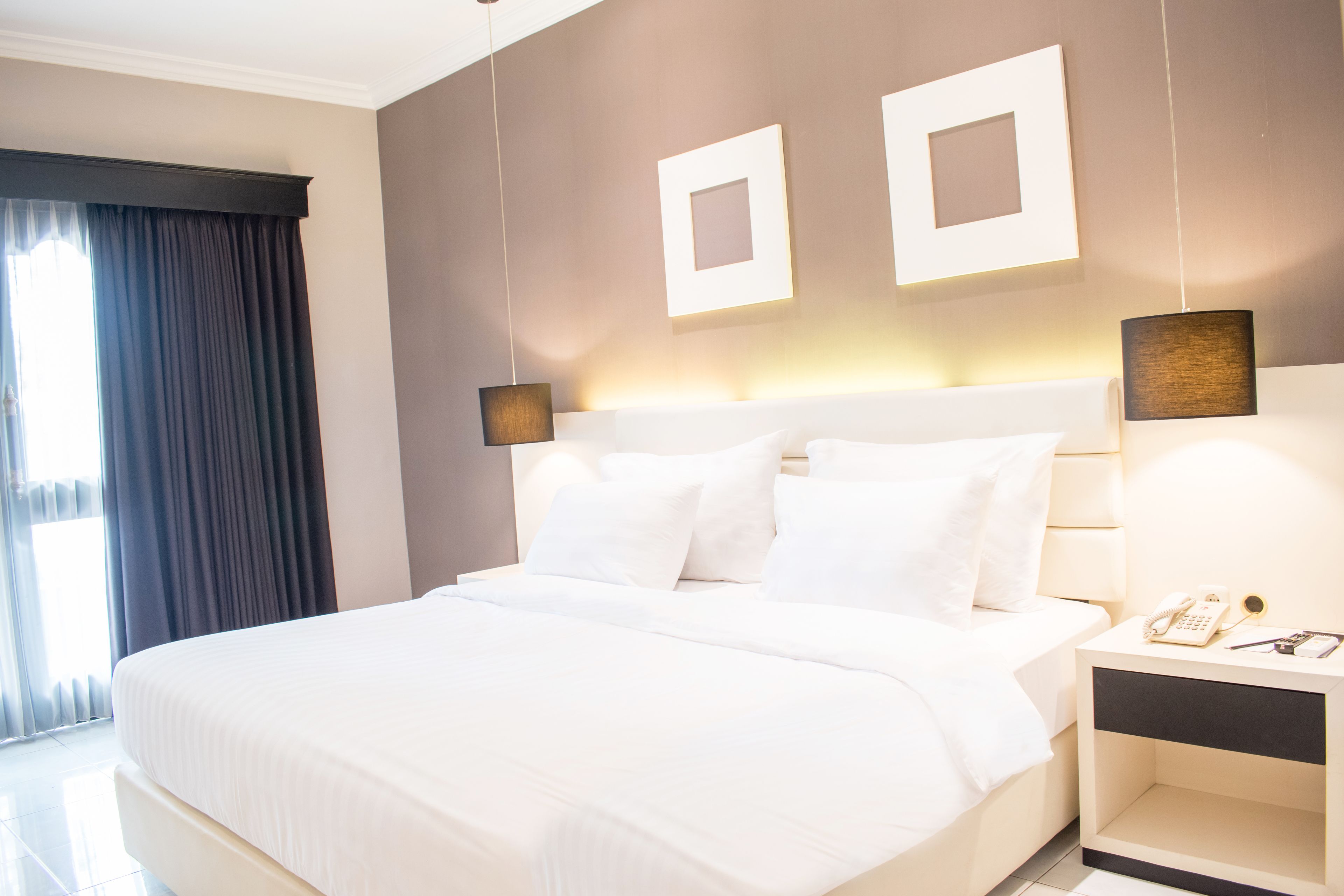A modern hotel room with a large bed, bedside tables, and a nightstand with a phone and glasses.