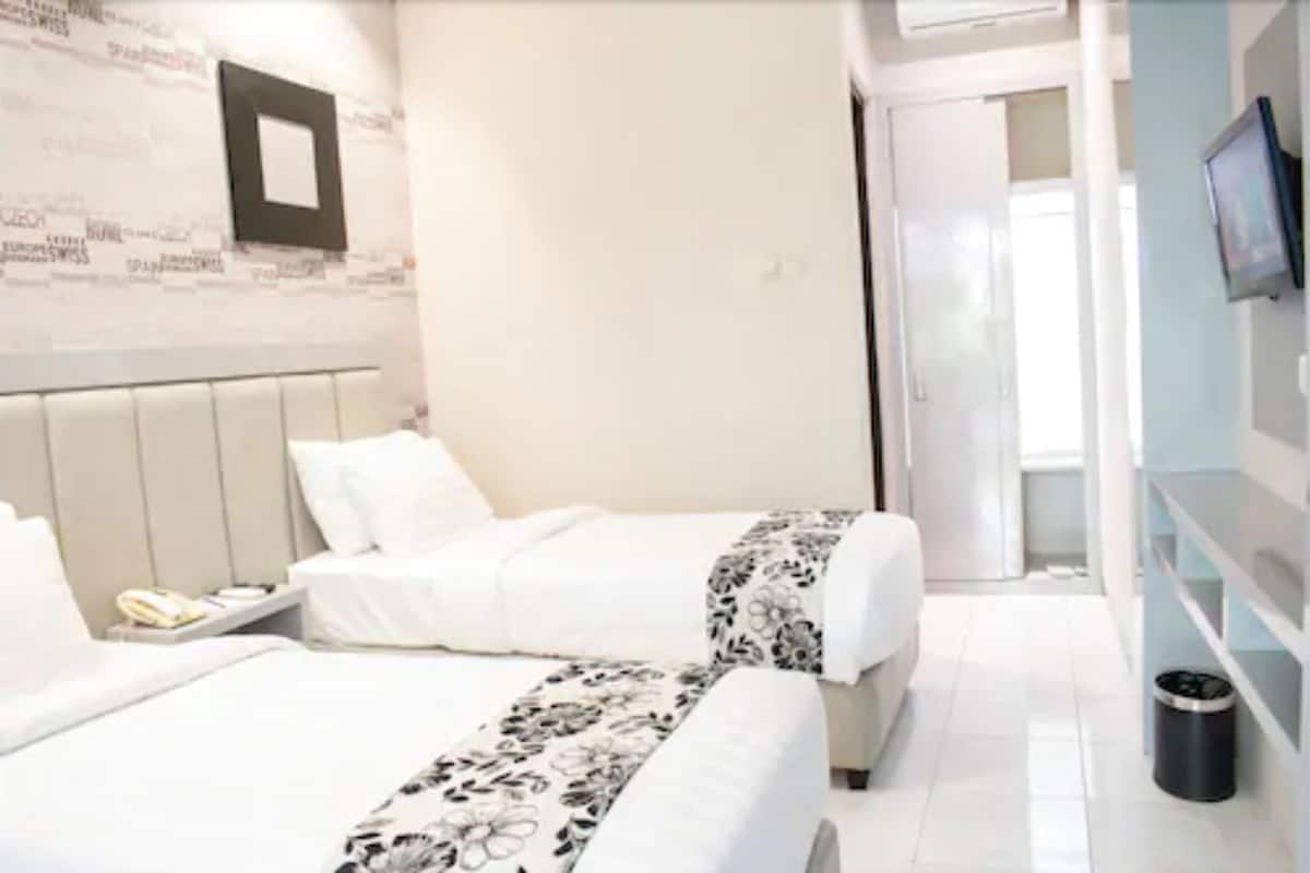 Habitación de hotel con dos camas, una mesita de noche con teléfono, televisor montado en la pared y un cubo de basura.