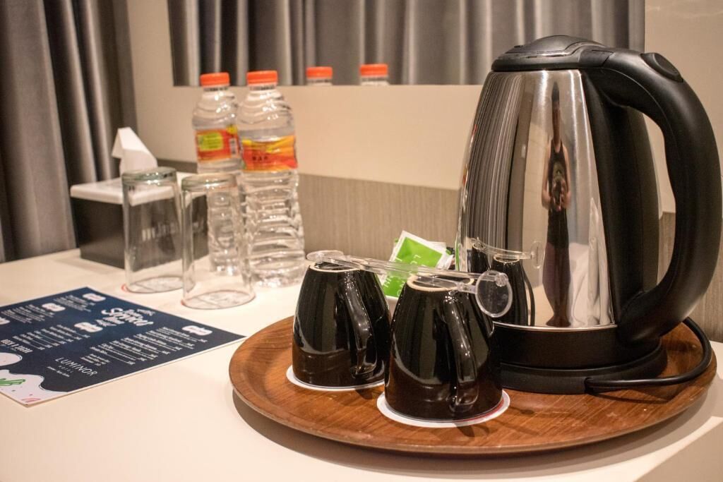 Un coin café comprenant une bouilloire, deux tasses et trois bouteilles d’eau, le tout disposé sur un plateau.
