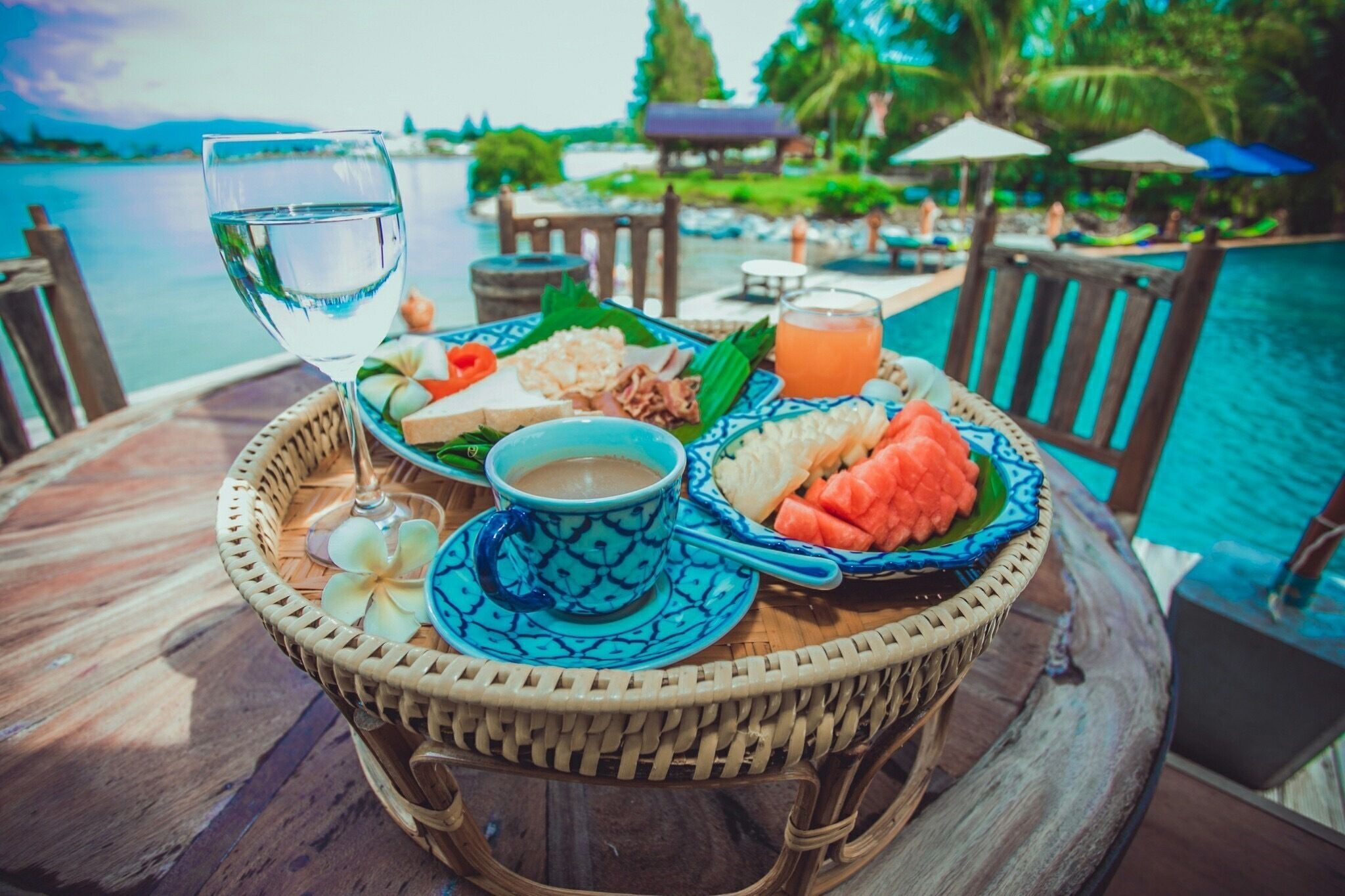 A table with a drink, a cup, and a plate with food by a poolside.
