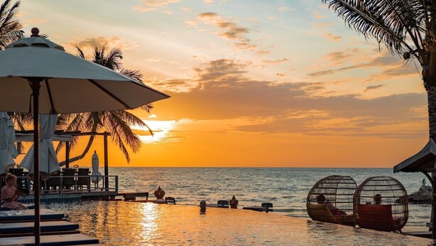 A resort pool area with lounge chairs and umbrellas, overlooking the ocean at sunset. - Sasitara   Thai  villas (Koh Samui)