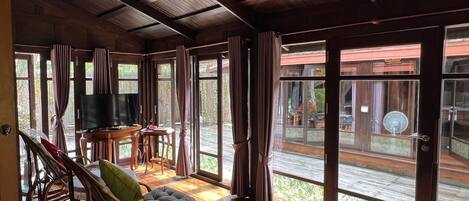 A spacious living area with a television, wicker furniture, and large sliding glass doors leading to an outdoor deck.